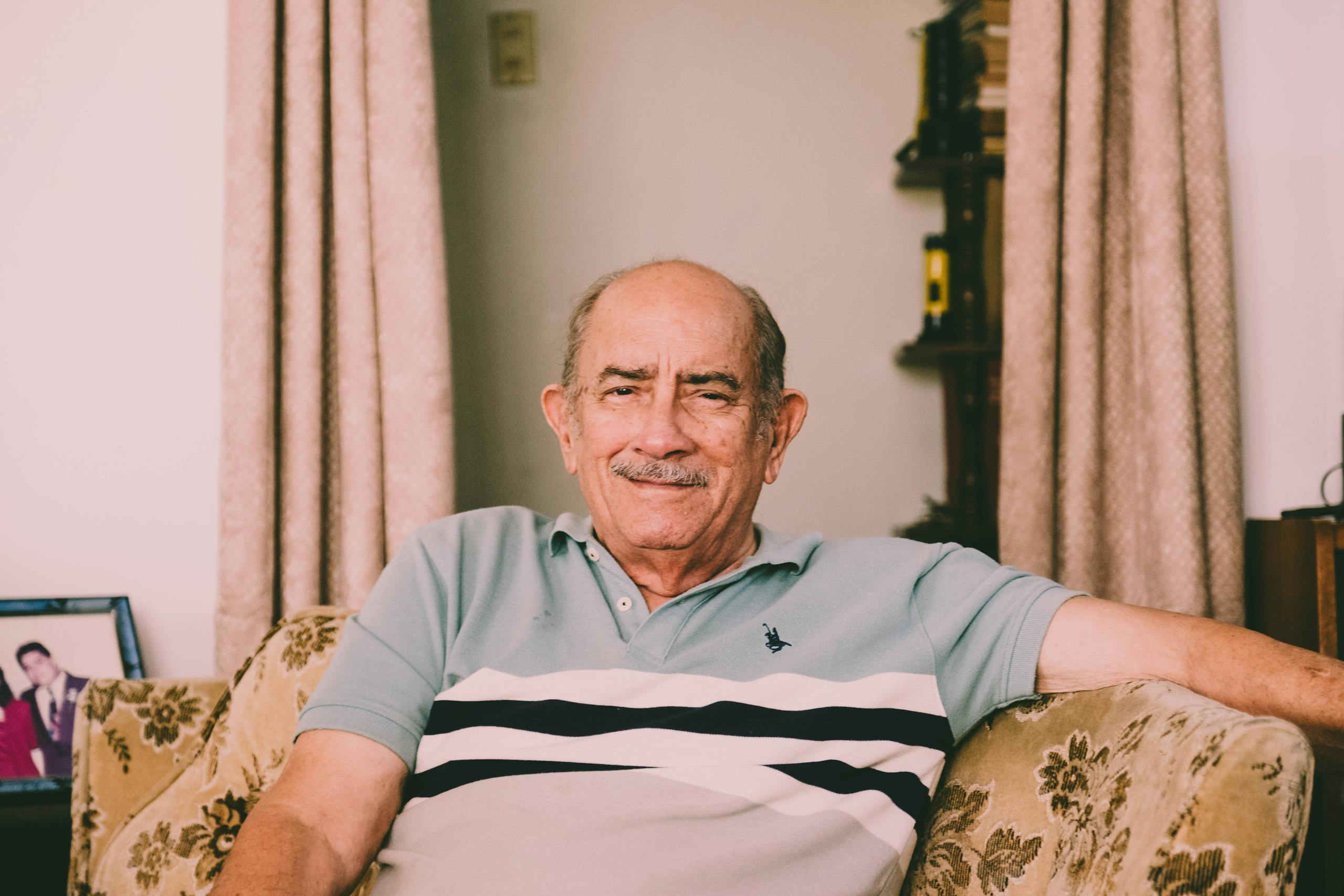 A cheerful elderly man enjoys a relaxed moment on a sofa in a warmly decorated living room.