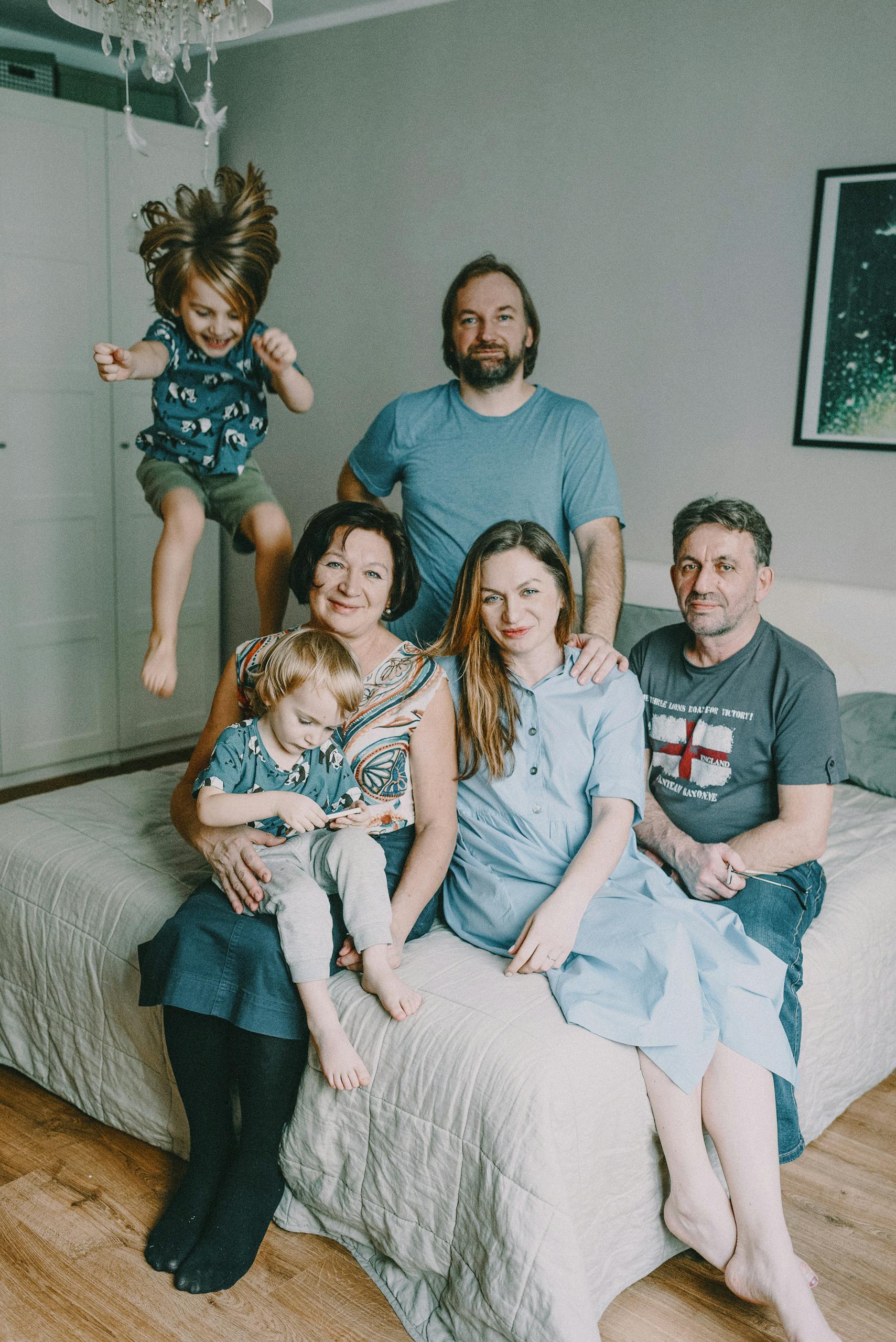 A cheerful multigenerational family posing together in a cozy bedroom setting.