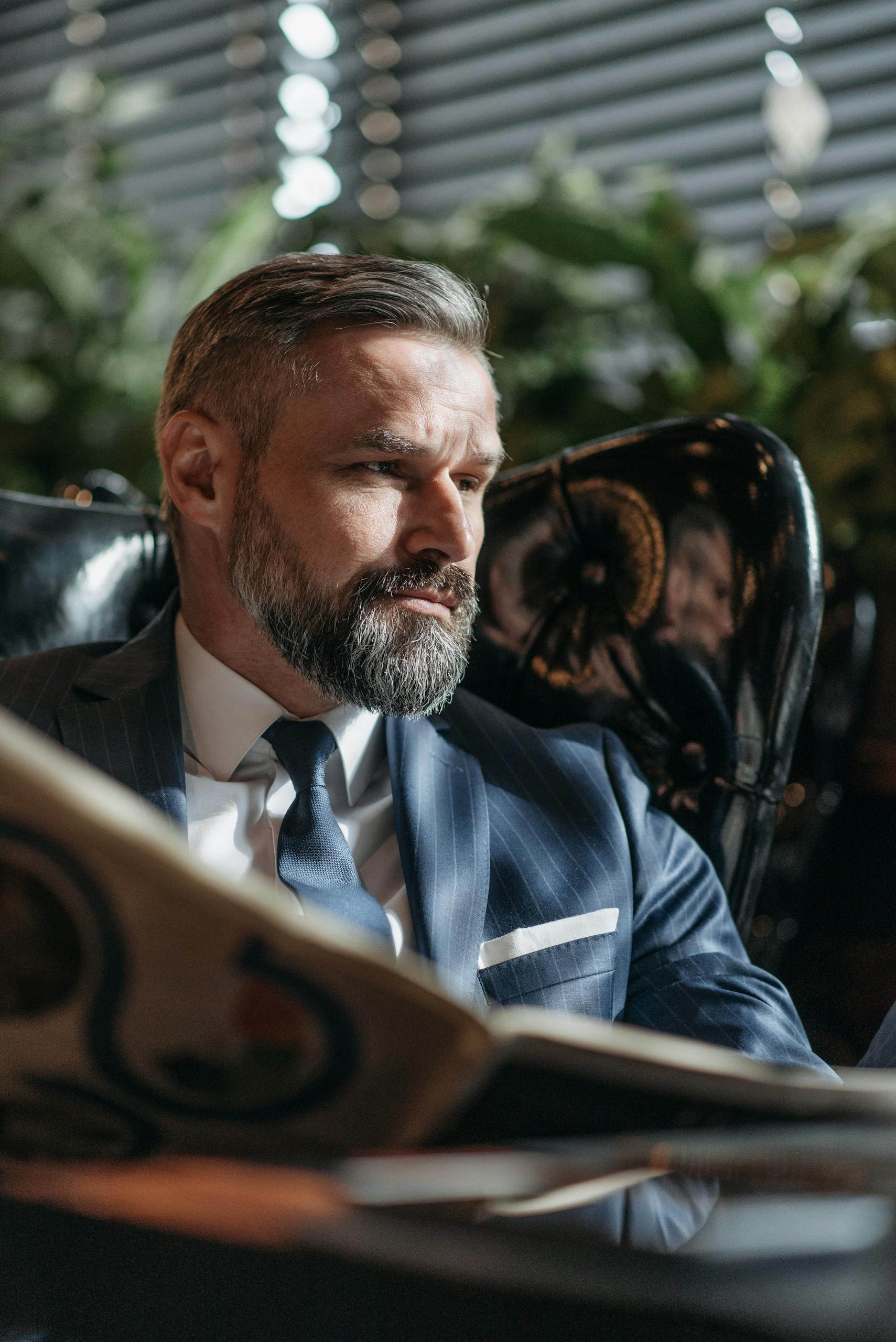 Professional businessman with beard reads a newspaper indoors in a formal setting.