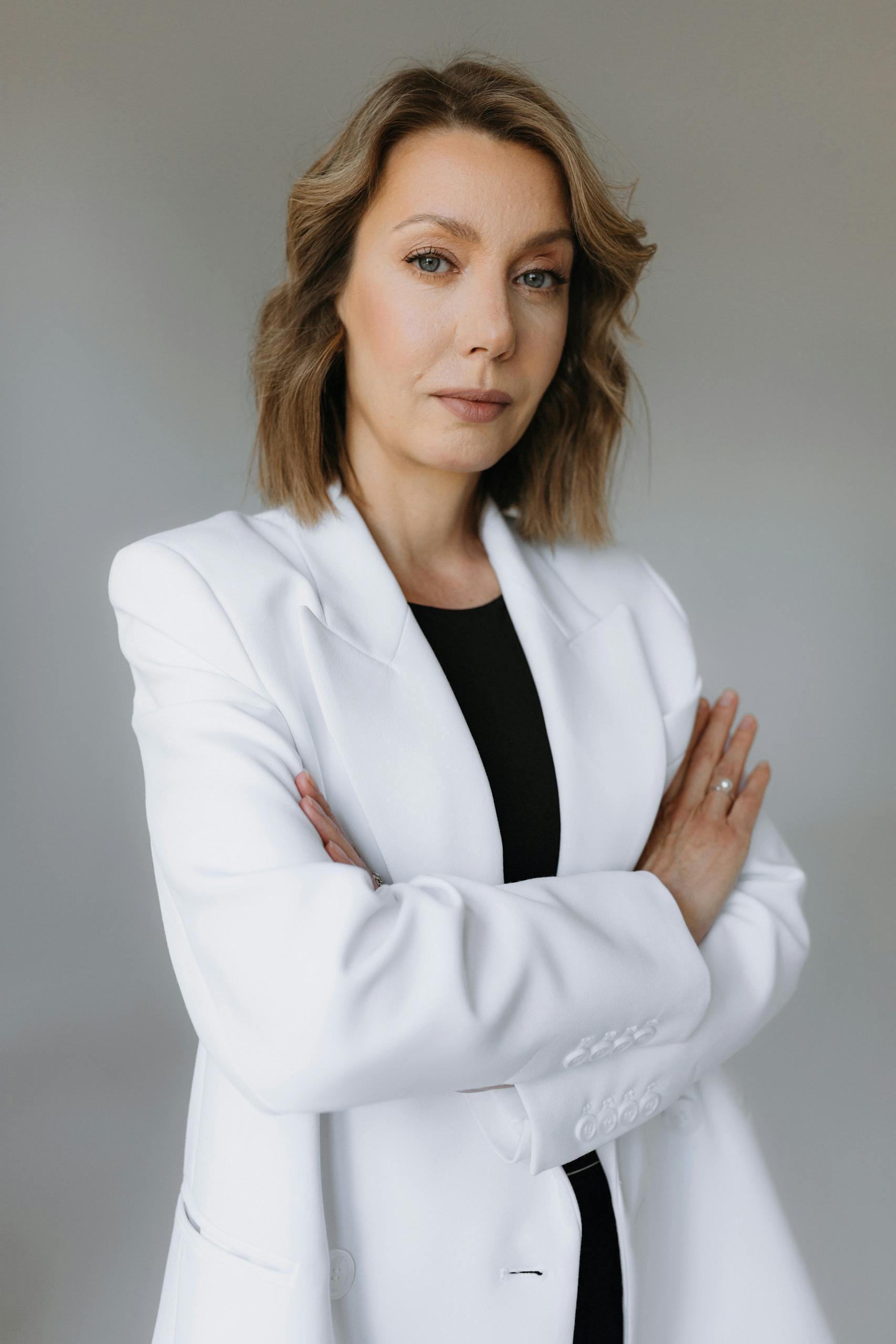 Professional woman posing confidently in a white suit against a neutral background.