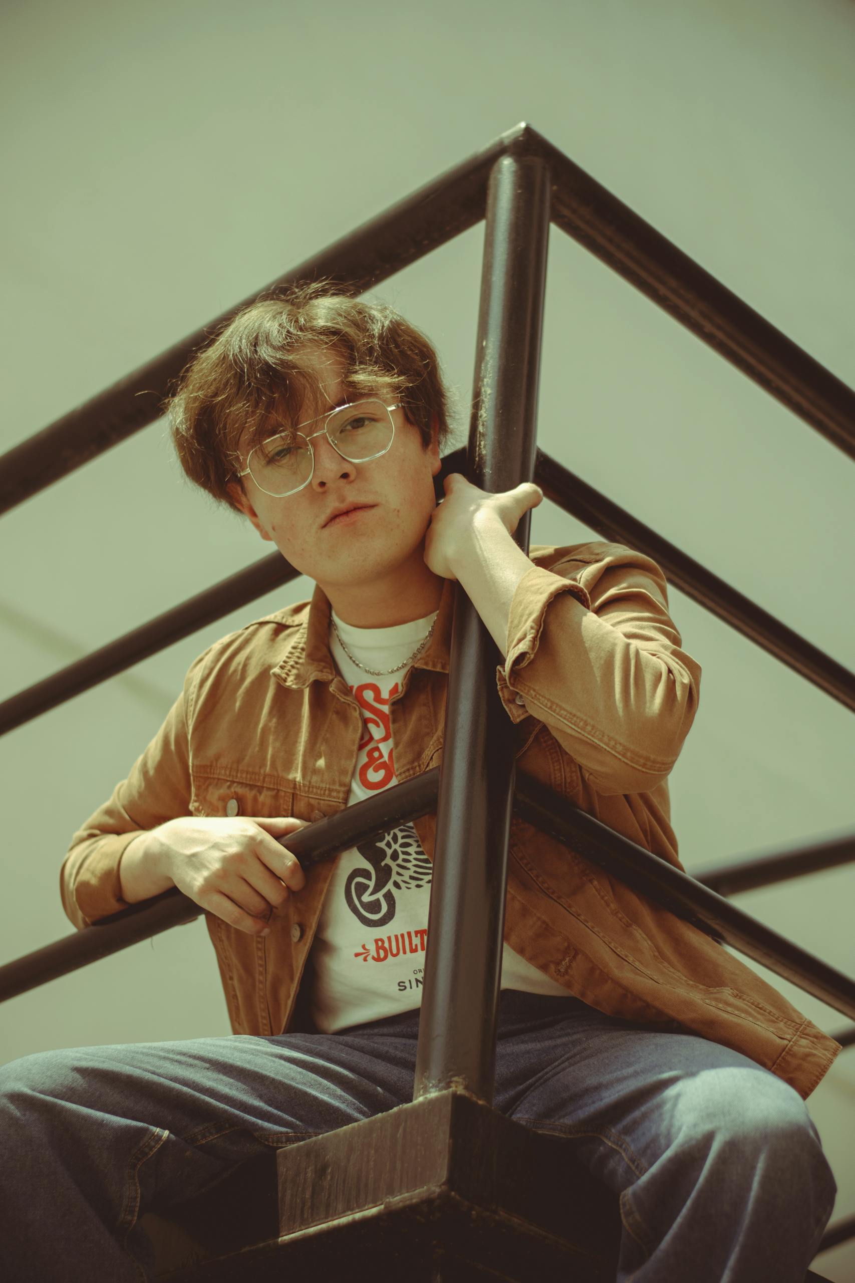 Relaxed portrait of a young adult in casual attire leaning on a stair railing outdoors