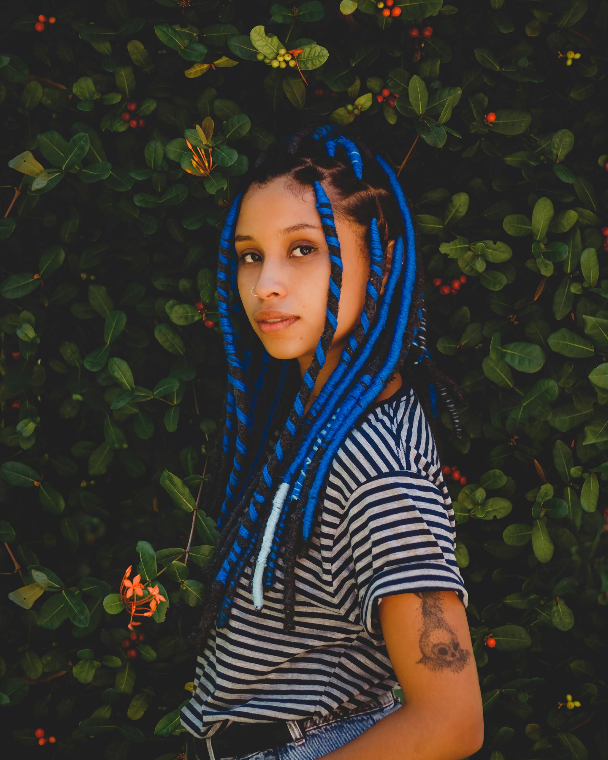 Young woman with blue braids posed outdoors with floral backdrop.